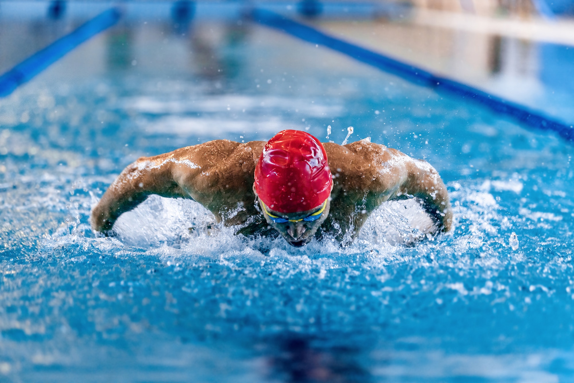 Front view of professional male swimmer in red cap and goggles in motion and action during training