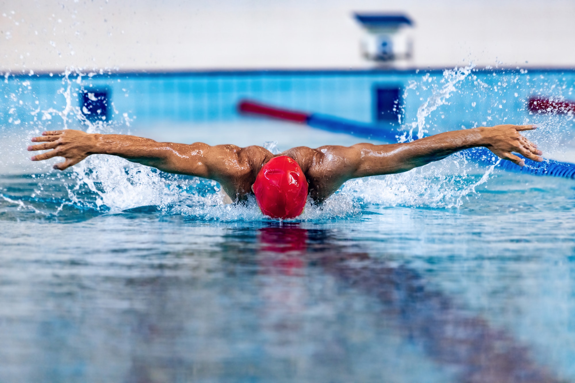 Professional male swimmer in swimming cap and goggles in motion and action during training at pool